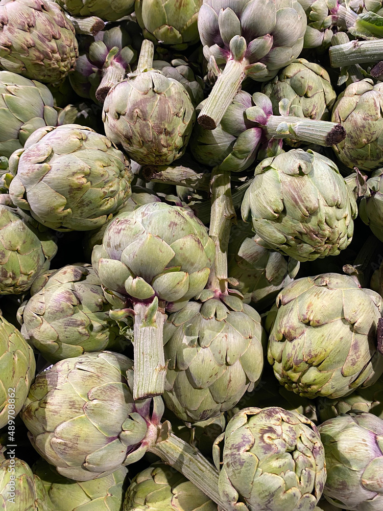 Obraz premium Organic raw artichokes in the grocery store. Vertical artichokes background. Vegetarian healthy food