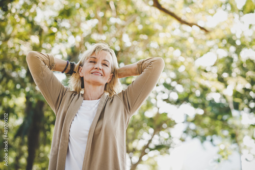 Portrait of happy elderly senior Caucasian woman do stretching and relaxing feel refresh and freedom breathing fresh air with sunlight enjoying a day in the outdoors park on summer