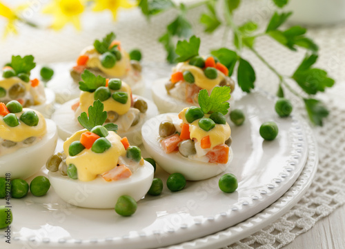 Easter boiled eggs stuffed with traditional vegetable salad with mayonnaise served on a white plate close up view