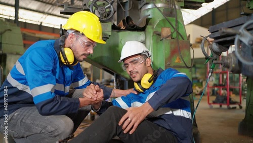 Man labor worker had accident and sit beside cutting equipment at the production line of CNC machine factory. Engineer man help and support him on injured. Safety in industrial factory. Injury at work