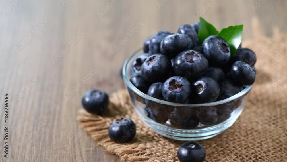 Pan motion from left to right of Blueberry with leaves in glass cup in wood table Pan motion from left to right of Blueberry with leaves in glass cup in wood table