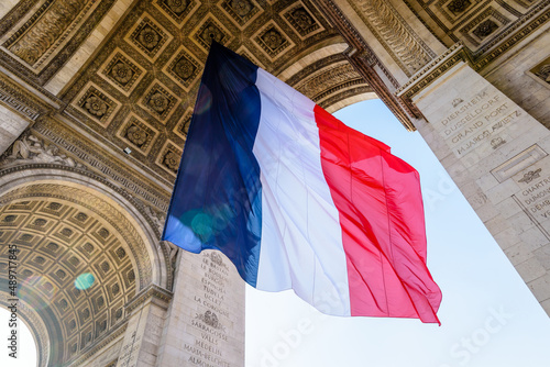 A large french flag is fluttering under the Arc de Triomphe in Paris, France.