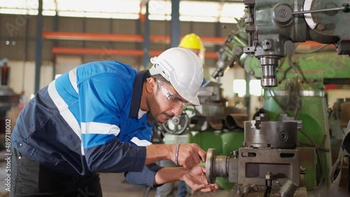 Engineer man check the operation of the equipment by turning part of machine at CNC factory. Worker wearing safety glasses and helmet. Maintenance, repairing and inspector concept. 