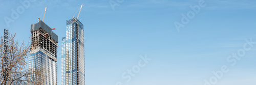 Construction of modern high-rise buildings. Two skyscrapers under construction against the blue sky. Banner format.