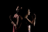 Fit couple posing together. Girl praying boy having fun. Side lit silhouettes on black background.