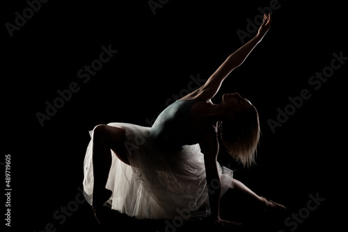 ballerina with a white dress and black top posing on black background. side lit silhouette.