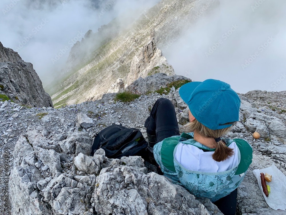 Woman eating lunch and looking down from peak in Austrian Alps. Vorarlberg, Austria.