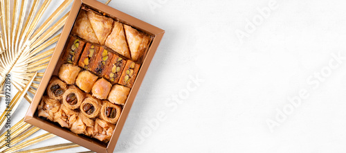 Web banner with collection of Eastern sweets in the golden box and copy space on white. Arabian baklava and ush-el-bul-bul dessert. Top view photo