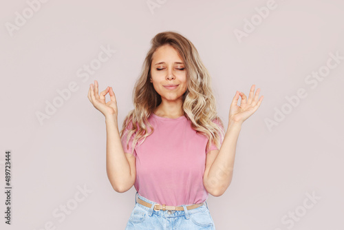 Wallpaper Mural A young caucasian pretty mindful blonde woman in a pink t-shirt keeps hands in mudra gesture with her eyes closed isolated on a pastel background. Peaceful girl meditates holding fingers in yoga sign Torontodigital.ca