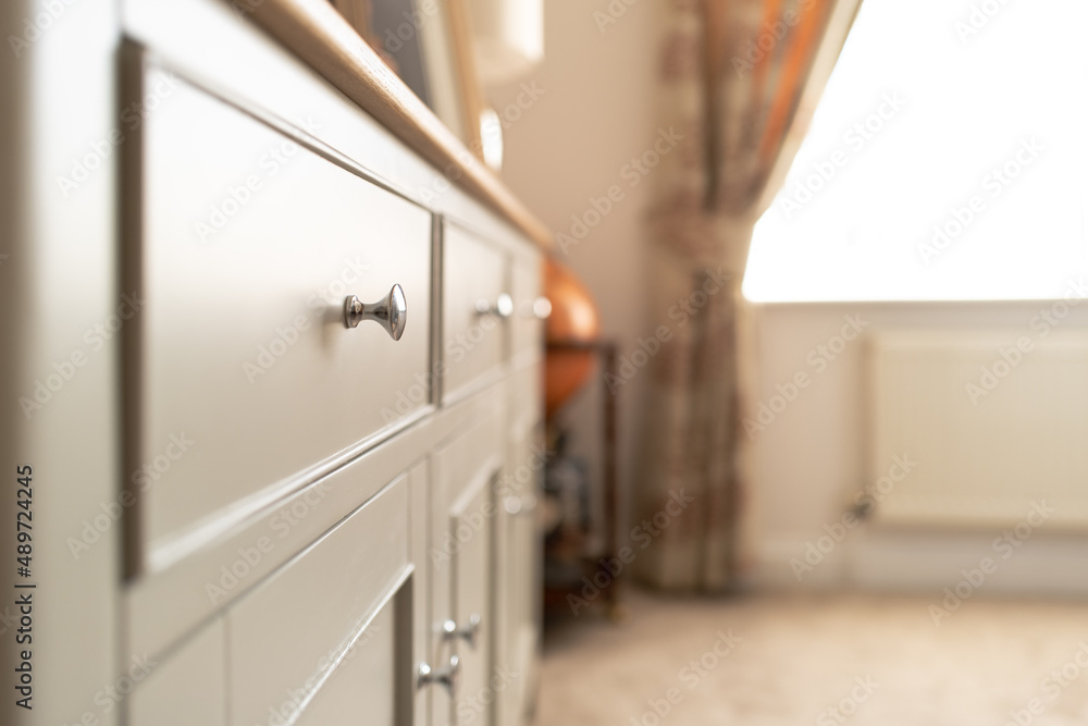 Shallow focus of a metal drawer knob seen on wooden sideboard furniture located in a light and comfortable dining room in a show home. Shallow focus of a metal drawer knob seen on wooden sideboard furniture located in a light and comfortable dining room in a show home.