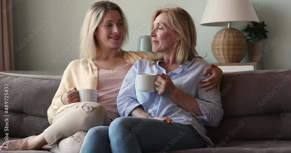 Young woman her older mom sit on sofa and talking, having pleasant conversation, enjoy beverage in cups take coffee break share news. Family bond, trust between mother and grown up daughter concept Young woman her older mom sit on sofa and talking, having pleasant conversation, enjoy beverage in cups take coffee break share news. Family bond, trust between mother and grown up daughter concept