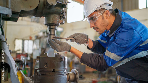 Engineer man checking the status of machine and used wrench to screw some part of equipment at CNC factory. Worker wearing safety glasses and helmet. Maintenance and repairing concept.