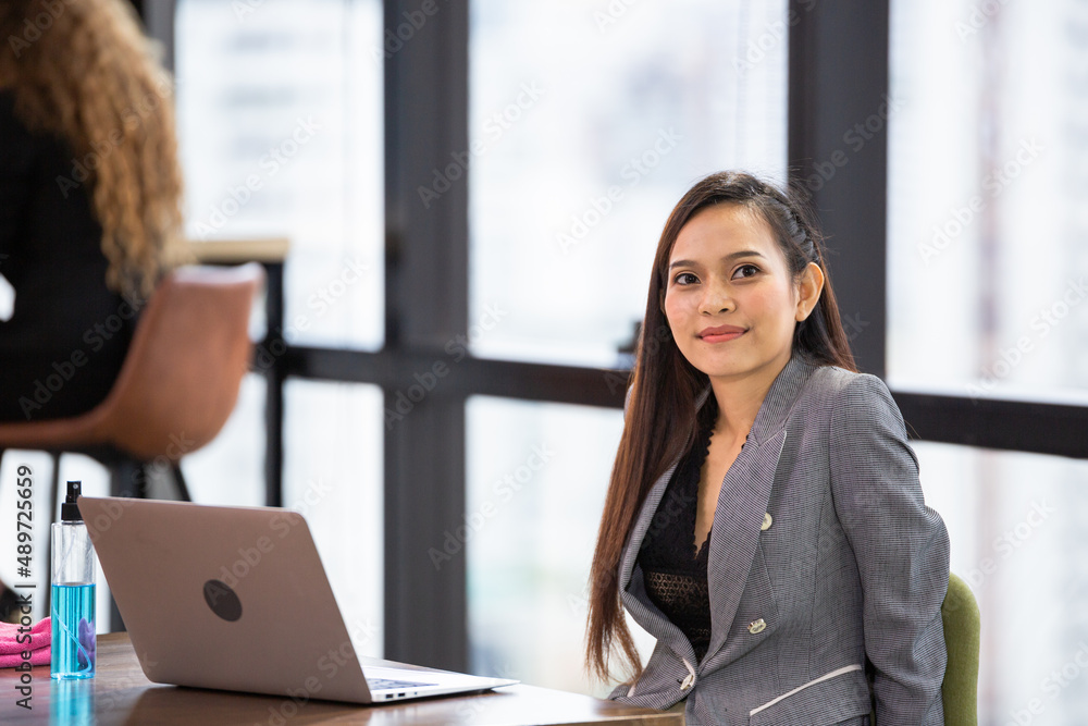 Asian female employee sitting at desk in the office looking at camera. corporate people working with computer laptop Asian female employee sitting at desk in the office looking at camera. corporate people working with computer laptop
