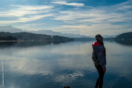 Happy woman standing on the pier at beautiful Woerthersee in Poertschach, Carinthia, Austria. Scenic lake landscape surrounded by Karawanks Alps. Fresh and clean air. Reflection in Lake Woerth