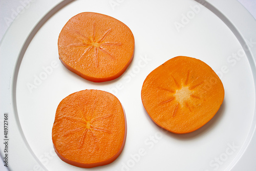 White dish with sliced juicy persimmon slices close-up
