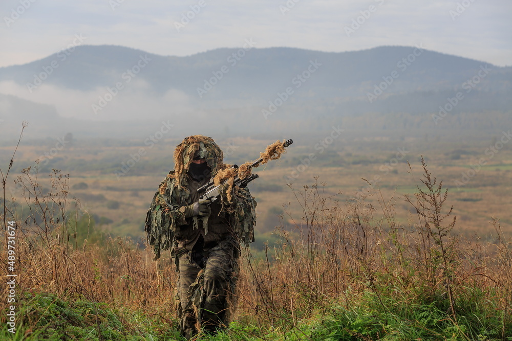 Sniper with Ghillies camouflage with sniper rifle with optics with empty landscape behind him, illustration photo for war Sniper with Ghillies camouflage with sniper rifle with optics with empty landscape behind him, illustration photo for war