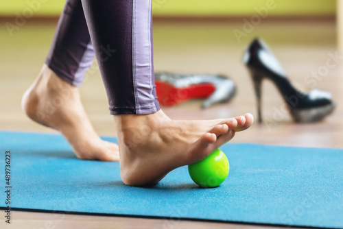 Myofascial relaxation of the hypermobile muscles of the foot with a massage ball, standing on a mat in the studio. Prevention of leg fatigue after wearing high-heeled shoes photo