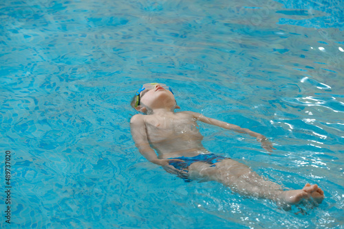 Boy floating on the back in the water in indoor swimming pool. Relaxing and balancing. Physical activity for toddler children Early development. Boy kid trained to kick legs. Copy space