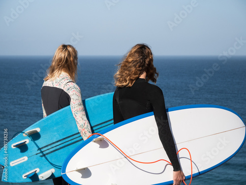 Unrecgonizable surfer women watching the ocean at the surf spot holding surfboards