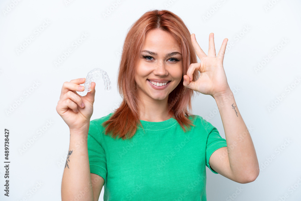 Young Russian girl holding invisible braces isolated on white background showing ok sign with fingers Young Russian girl holding invisible braces isolated on white background showing ok sign with fingers