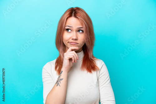 Young Russian woman isolated on blue background having doubts and thinking