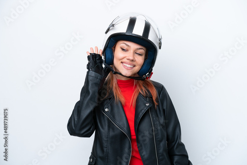 Young Russian girl with a motorcycle helmet isolated on white background listening to something by putting hand on the ear