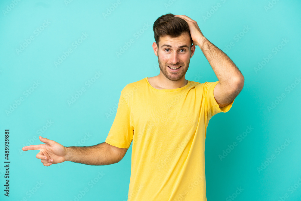 Young caucasian handsome man isolated on blue background surprised and pointing finger to the side Young caucasian handsome man isolated on blue background surprised and pointing finger to the side