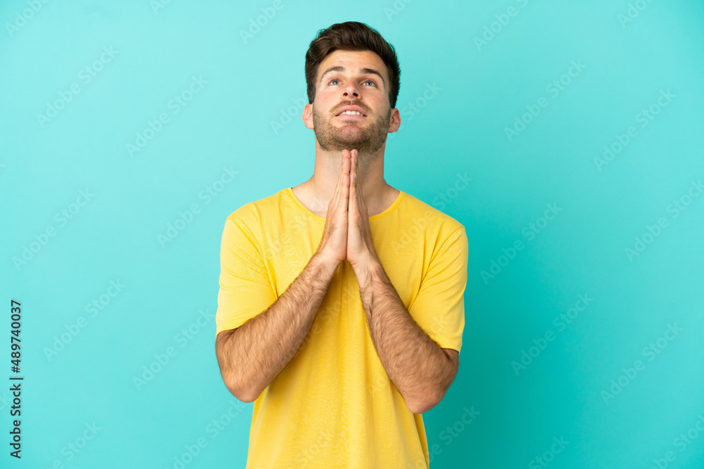Young caucasian handsome man isolated on blue background keeps palm together. Person asks for something Young caucasian handsome man isolated on blue background keeps palm together. Person asks for something