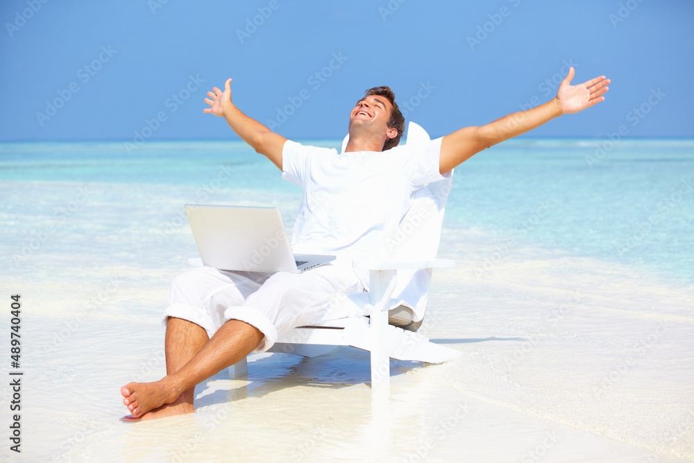 Away from hectic life. Portrait of carefree man outstretching his arms with laptop on beach.