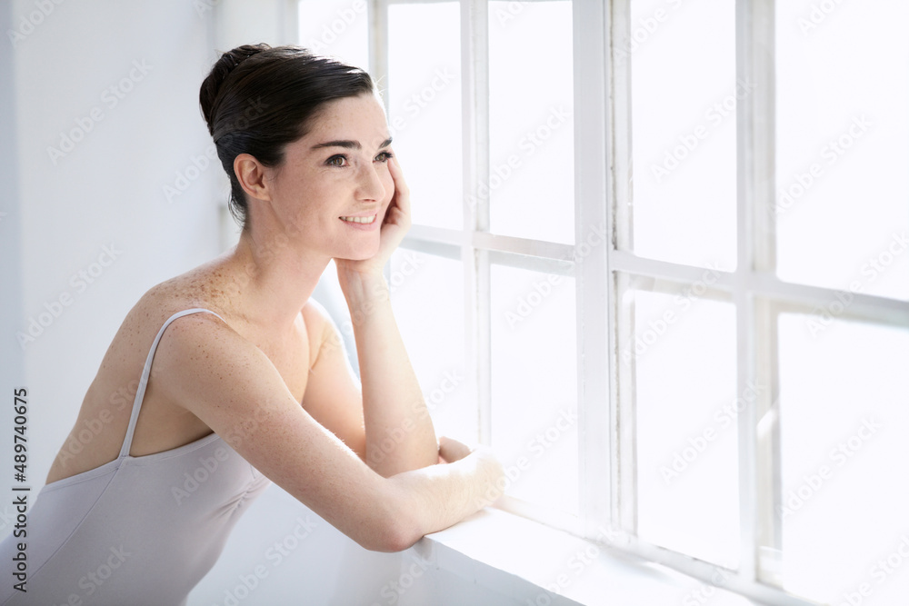 One day Ill be the prima ballerina. Smiling young ballerina looking out of a window.