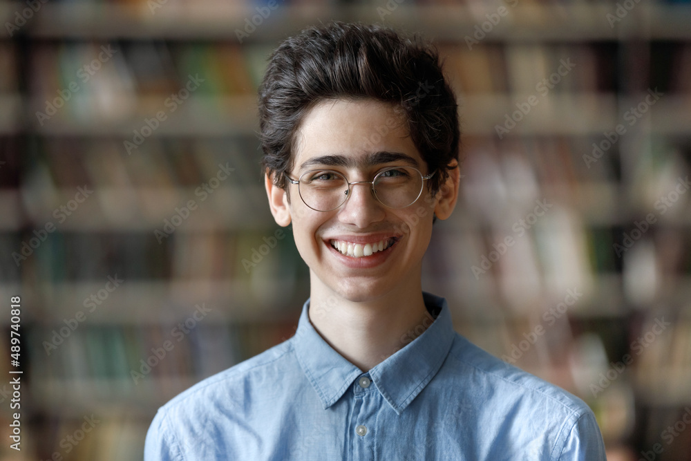 Head shot portrait of happy handsome Jewish male student in eyeglasses posing at blurred library background. Smiling Z generation smart guy looking at camera, high school or college education concept. Head shot portrait of happy handsome Jewish male student in eyeglasses posing at blurred library background. Smiling Z generation smart guy looking at camera, high school or college education concept.