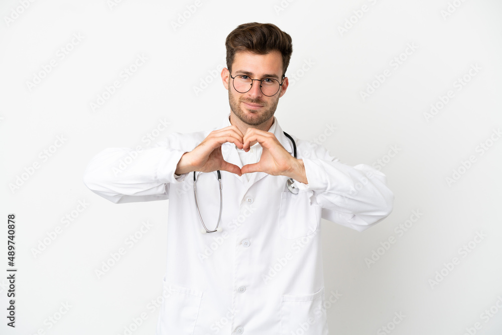 Young doctor caucasian man over isolated on white background wearing a doctor gown making a heart with hands Young doctor caucasian man over isolated on white background wearing a doctor gown making a heart with hands