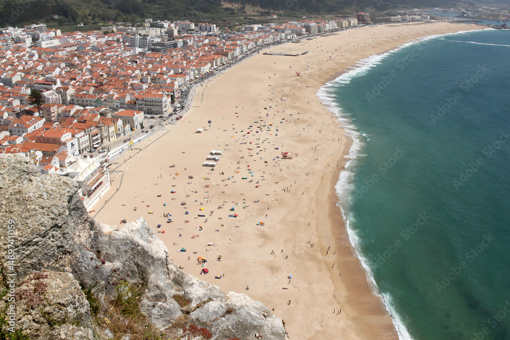 View of the beautiful sandy beach and white houses with clay tiled roofs on the Atlantic ocean coast from the cliffs above Nazare , Portugal
