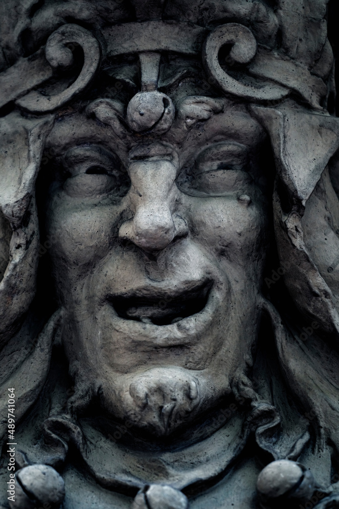Evil clown and crazy joker. Fragment of an ancient stone statue. Close up.