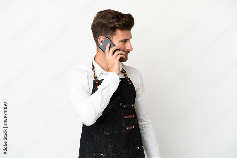 Restaurant caucasian waiter isolated on white background keeping a conversation with the mobile phone with someone Restaurant caucasian waiter isolated on white background keeping a conversation with the mobile phone with someone
