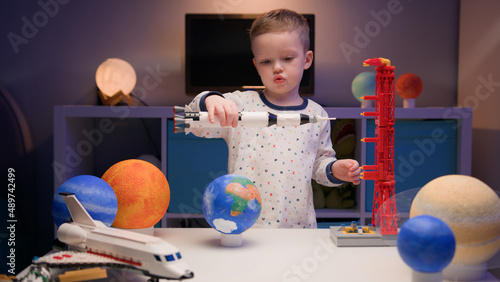 Little blonde boy kid plays with spaceship from constructor, flies near planets of solar system in evening. Child imagines himself as pilot of spaceship. Desire fly in space, flying on spaceship.