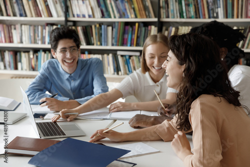 Fotografia Distracted from preparing college project happy young laughing diverse classmates having fun, telling jokes, enjoying carefree pause time together, sitting at table in library, friendly communication