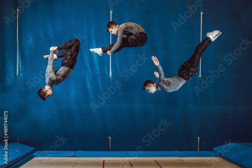 Youn man doing different pirouettes in elastic bed in mid-air. Blue background, collage