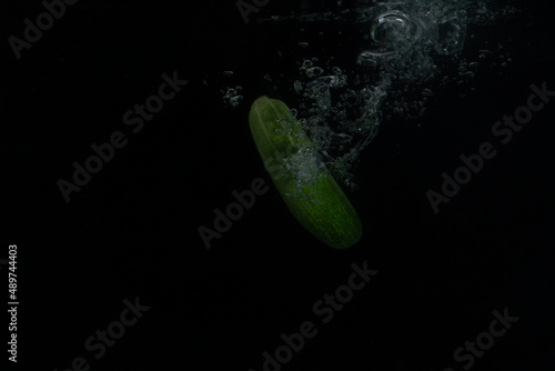 cucumber falling into water with splash on black background