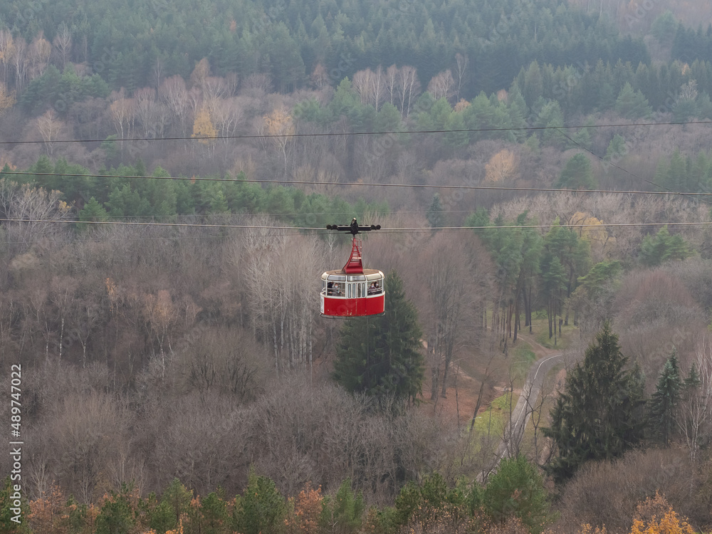 Fototapeta premium A red retro style cable car rides over a huge park area. Resort Kislovodsk park in autumn