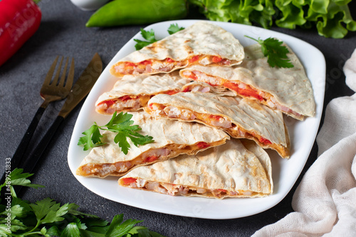 Mexican snack quesadilla from tortilla with bacon, chicken, cheese and pepper in white plate on gray background