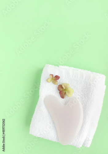 Top view of pink heart shaped guasha stone made of quartz crystal on background with copy space. Concept of alternative skin care treatment, self massage and acupressure
