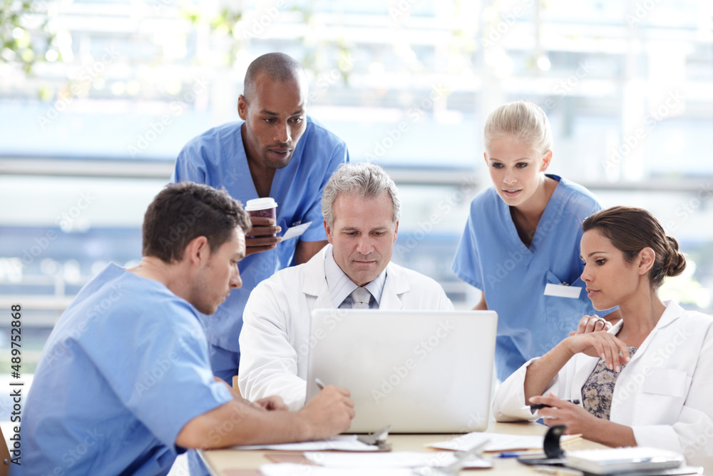 Dedicated team of healthcare professionals. A team of medical professionals working around a laptop. Dedicated team of healthcare professionals. A team of medical professionals working around a laptop.