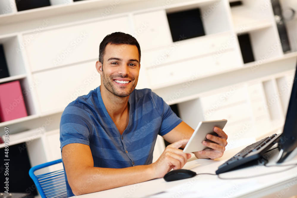 His business is boosted by his touchscreen. A smiling young casually-dressed entrepreneur working on his digital tablet. His business is boosted by his touchscreen. A smiling young casually-dressed entrepreneur working on his digital tablet.
