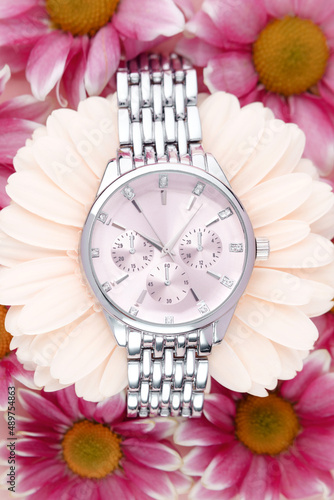 Women's wristwatch with silver strap and pink dial lies surrounded by purple flowers