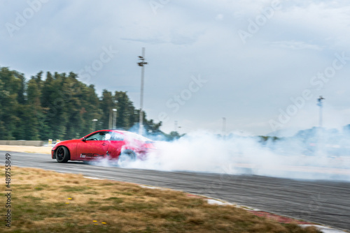 Red Drift Car / Race car drifting around corner very fast with lots of smoke from burning tires on speedway / racetrack / drift track. Infiniti g35 v8. JDM car. Luxury red sport car.