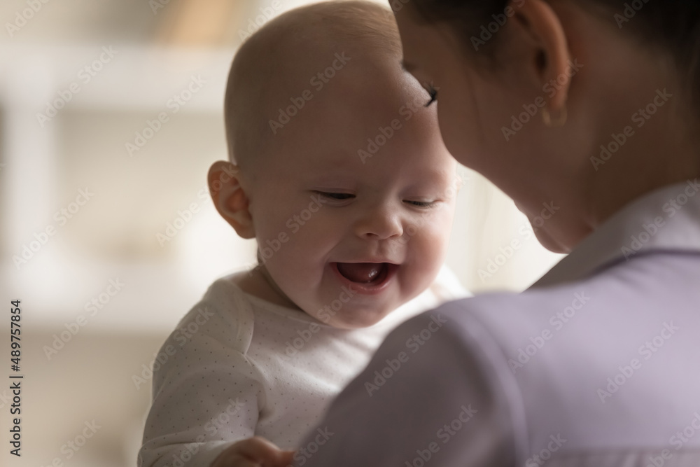 Happy cheerful adorable baby laughing, smiling in young mothers arms. New mom holding little kid, hugging positive child with tenderness, love, care. Close up. Motherhood concept Happy cheerful adorable baby laughing, smiling in young mothers arms. New mom holding little kid, hugging positive child with tenderness, love, care. Close up. Motherhood concept