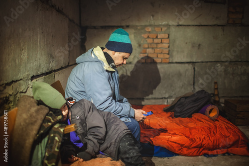 Terrorism and war, current history. Ukrainian father with little son sits in a bomb shelter, waits for the end of the air attack of Russian invaders and reads the latest braking news with smartphone © Maria