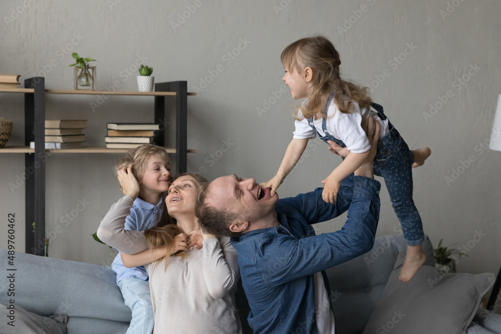 Φωτογραφία Cheerful happy parents cuddling, tickling excited giggling little preschool kids on couch