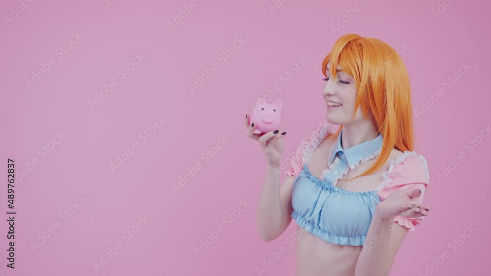 sweet caucasian teenage cosplayer shaking piggy bank and boasting she has more money now pink background studio shot. High quality 4k footage sweet caucasian teenage cosplayer shaking piggy bank and boasting she has more money now pink background studio shot. High quality 4k footage